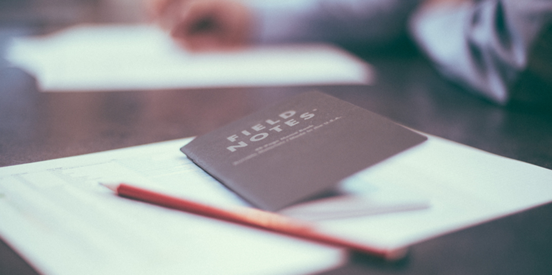 Photograph of a field notes notebook and a pencil on top of a sales report