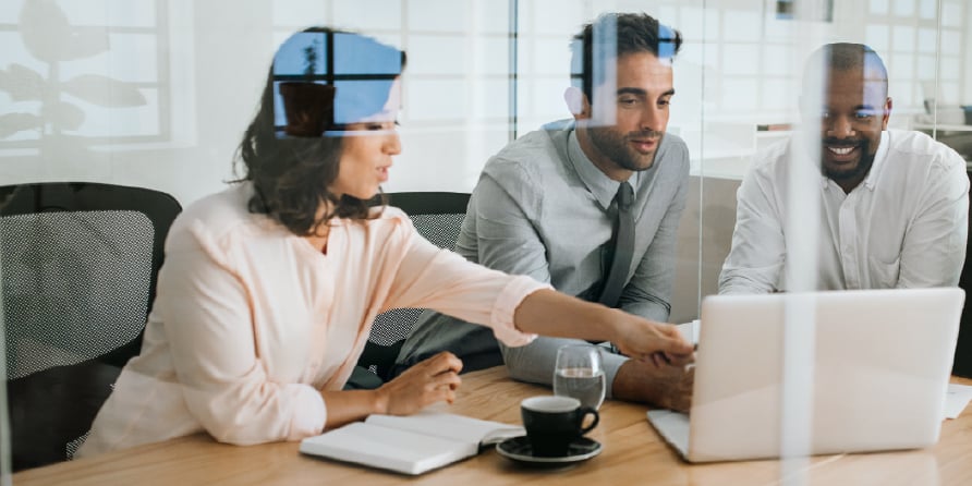 Photograph of three revenue leaders in front of a laptop on a conference table discussing sales cycle stages