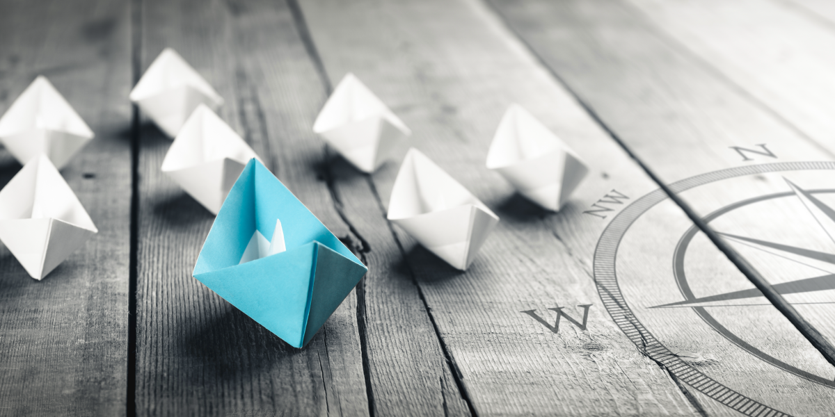 Stylized photograph of origami boats on a wood plank surface with a compass graphic overlaid