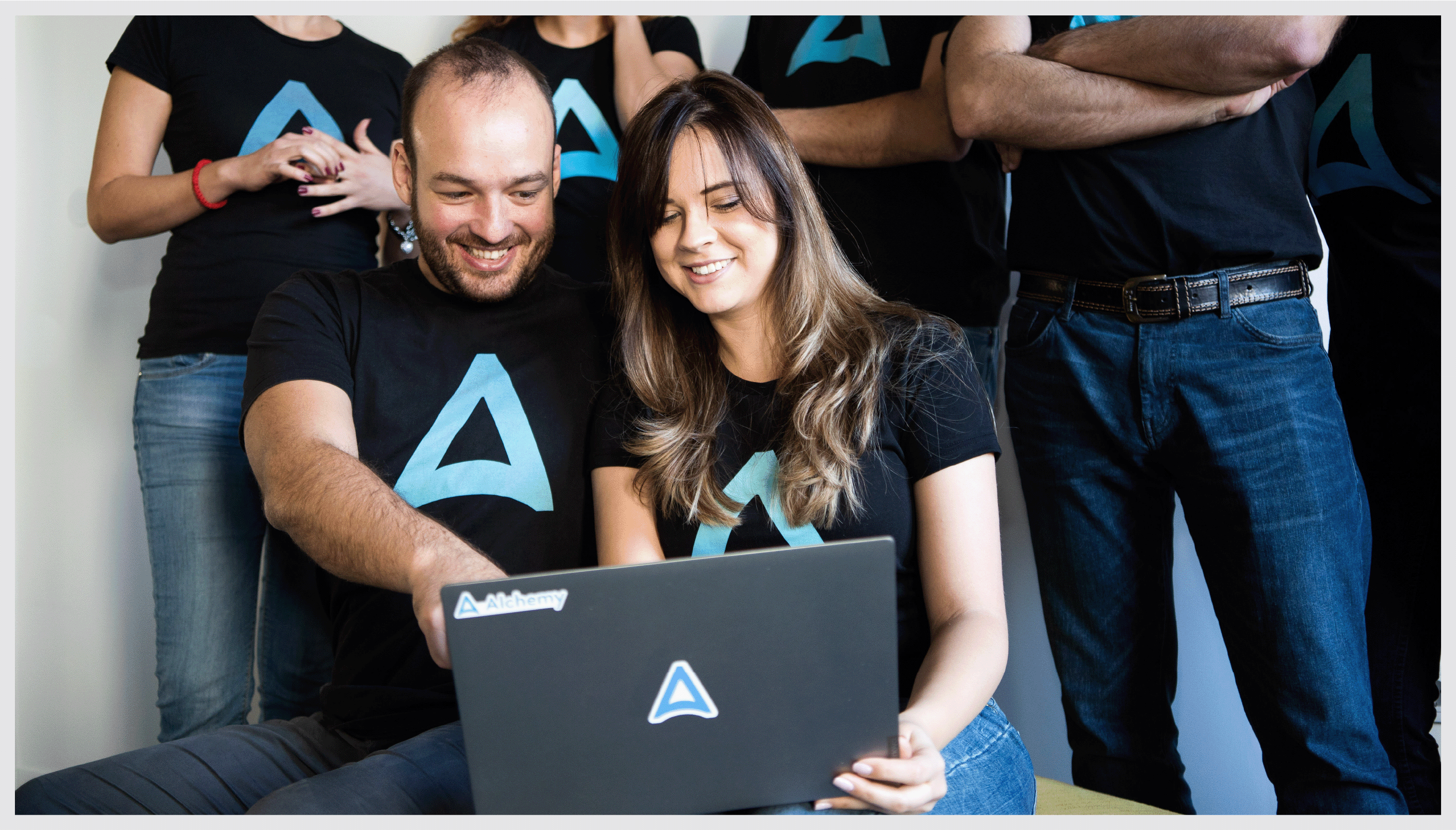 Photograph of a diverse group of Alchemy employees looking at a laptop screen